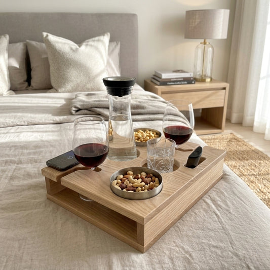 Wooden tray with wine glasses, snacks, and a phone on a bed in a bedroom setting.