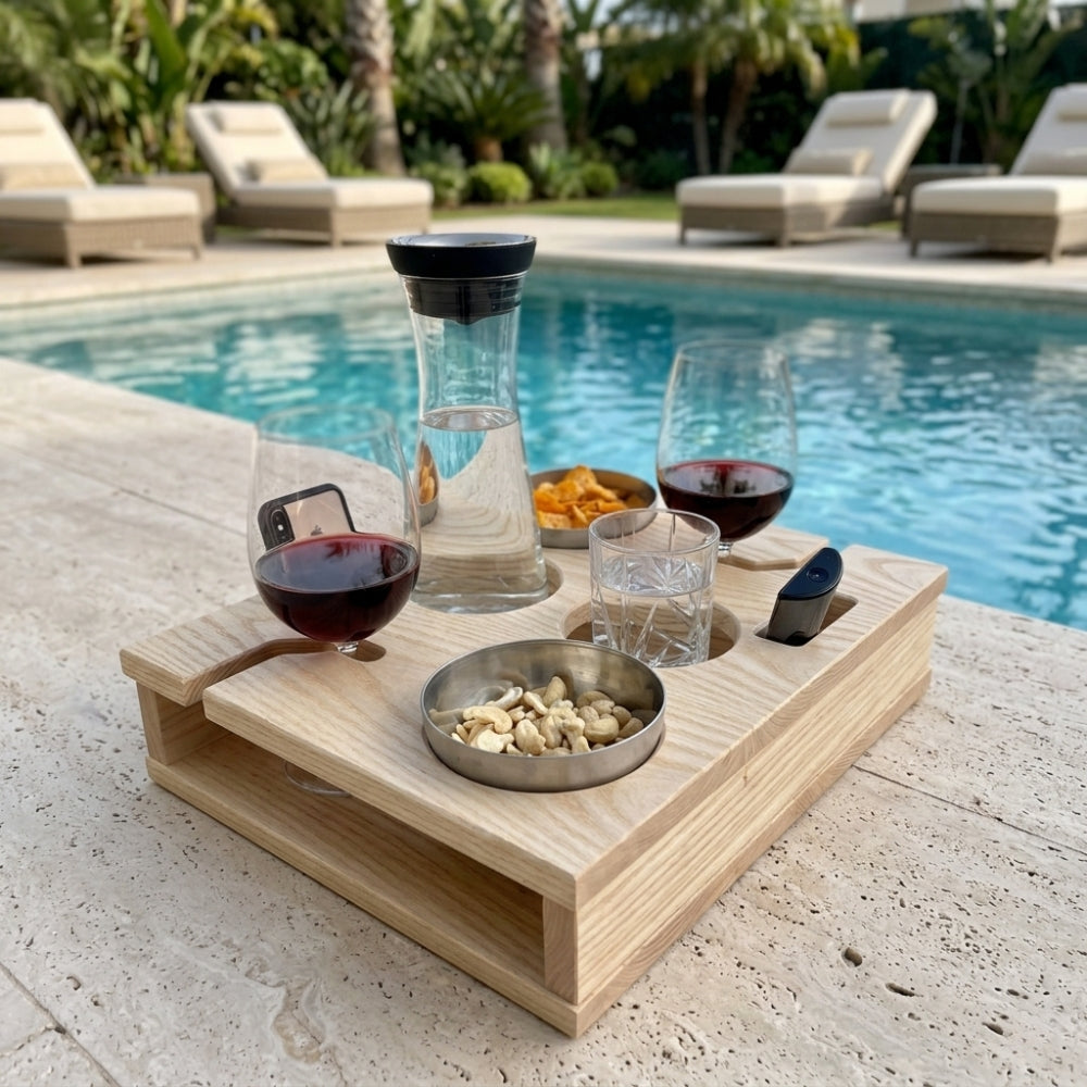 Wooden tray with wine glasses, snacks, and a carafe by a poolside