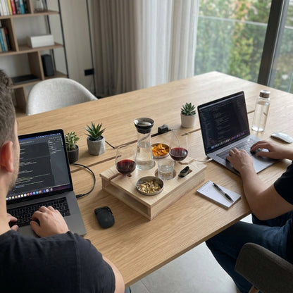 Two people working on laptops at a wooden table with snacks and drinks.