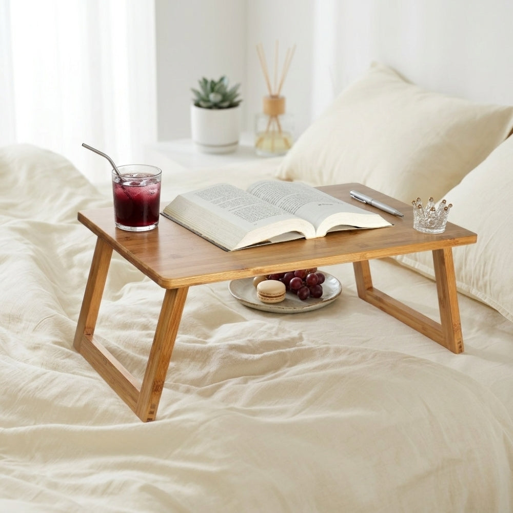 Wooden lap desk on a bed with a book, glass of juice, and plate of grapes.