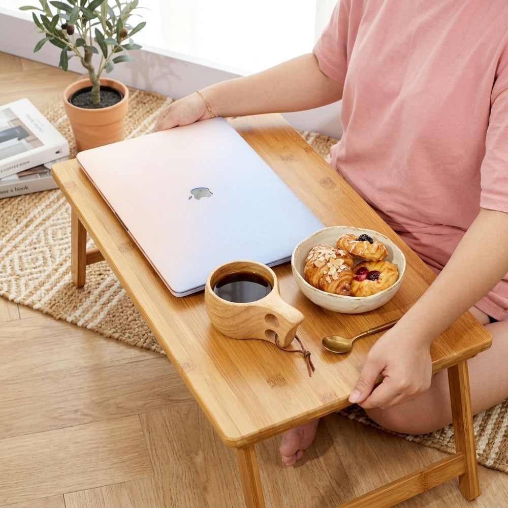 Person using a laptop on a small wooden table with a bowl of pastries and a cup of coffee.
