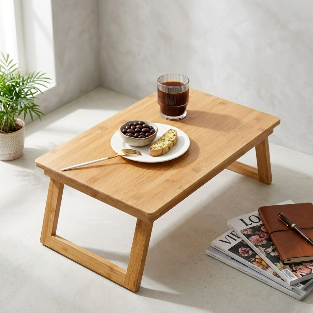 Wooden lap desk with a cup of coffee, plate of snacks, and a notebook on a light-colored floor.