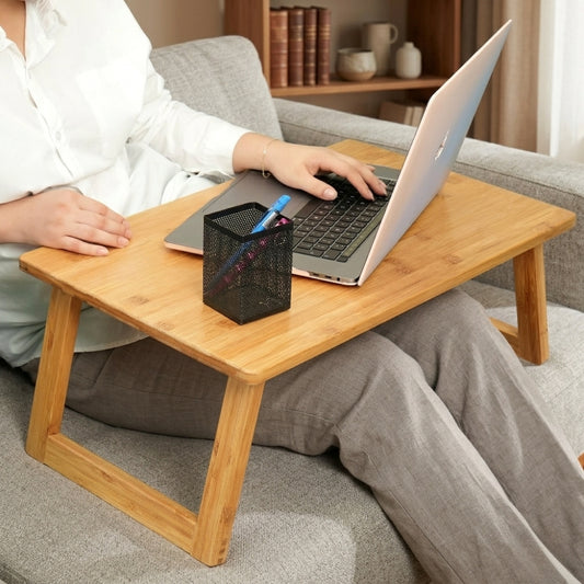 Person using a laptop on a wooden tray while sitting on a couch.