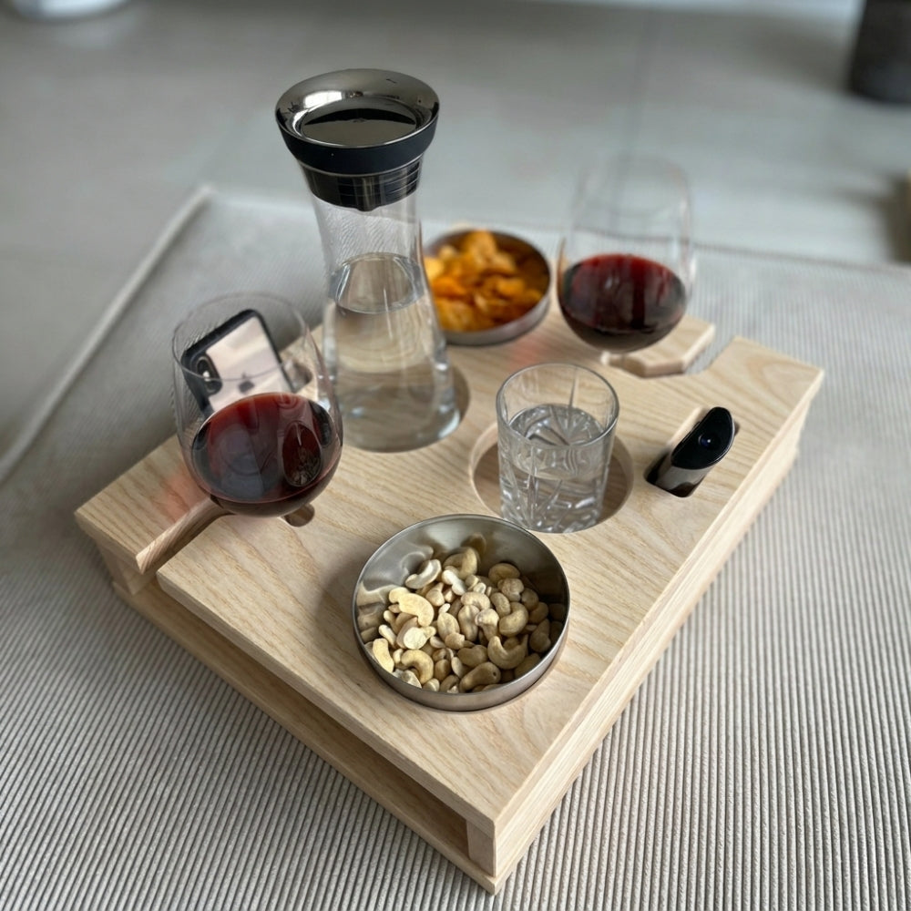 Wooden tray with wine glasses, a carafe, and snacks on a light surface.