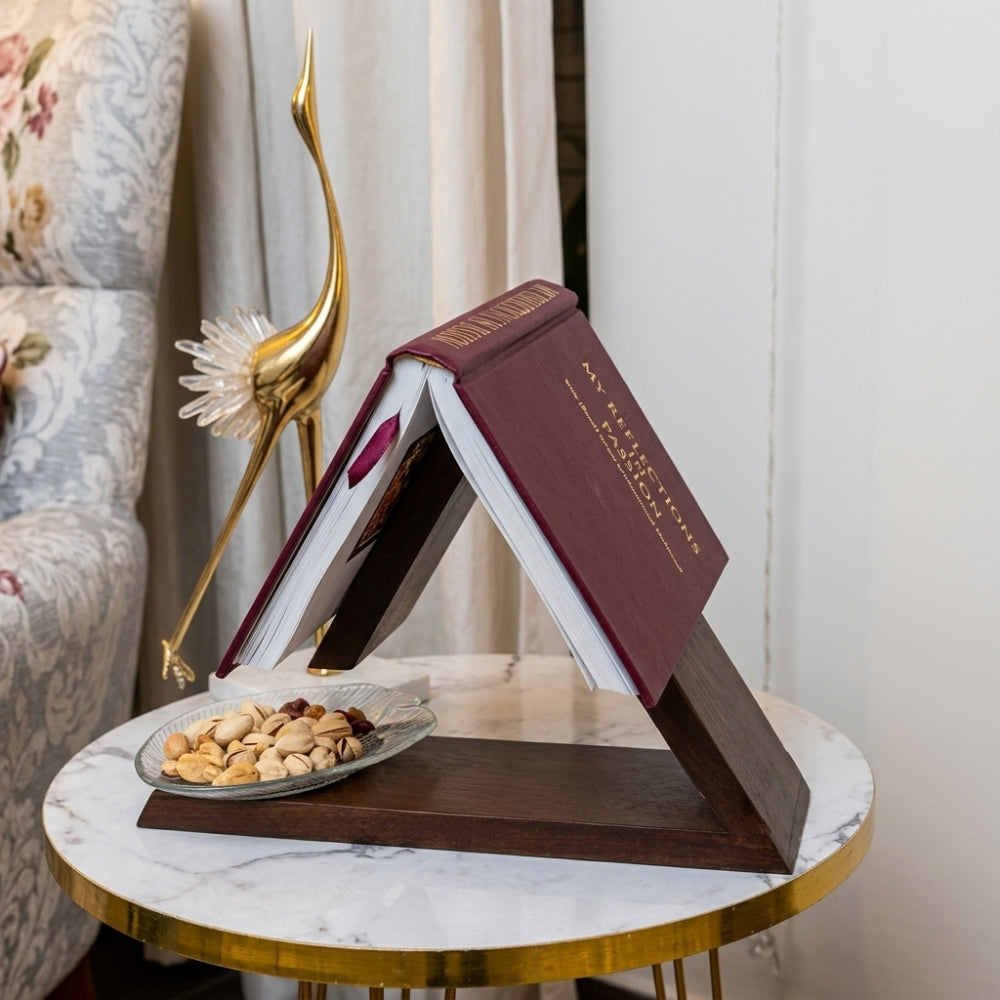 Decorative book stand with a book on a marble table, next to a plate of nuts.