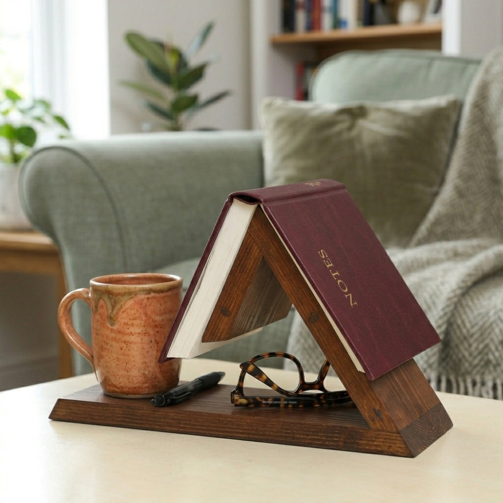 Wooden book stand with a book, mug, pen, and glasses on a table in a cozy living room.